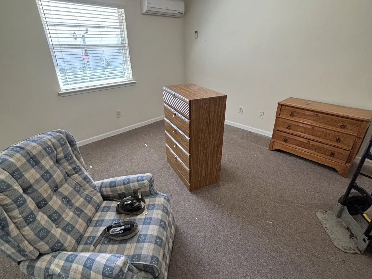 A bedroom with a plaid recliner and two wooden dressers before furniture removal